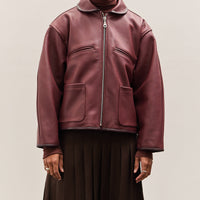 Person wearing a burgundy leather jacket on a plain background