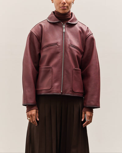 Person wearing a burgundy leather jacket on a plain background