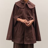 Person wearing a brown cape over a matching outfit against a plain background