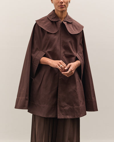 Person wearing a brown cape over a matching outfit against a plain background