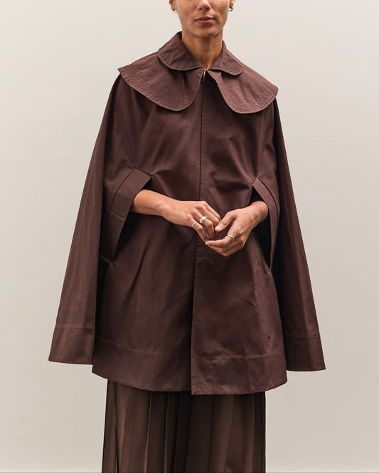 Person wearing a brown cape over a matching outfit against a plain background
