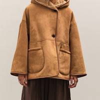Person wearing a brown shearling coat and hat on a plain background