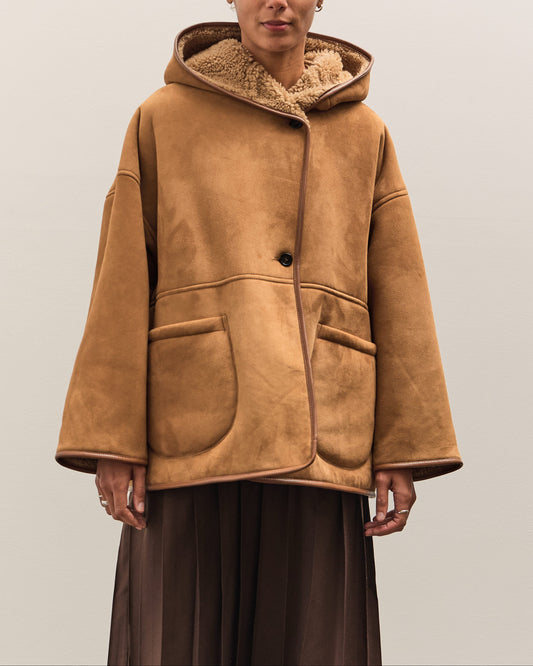 Person wearing a brown shearling coat and hat on a plain background