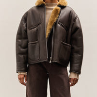Person wearing a brown leather jacket with fur trim on a plain background