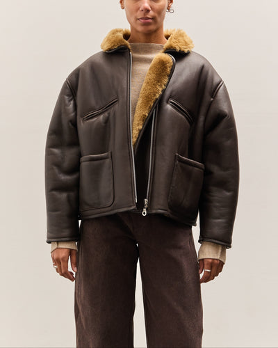 Person wearing a brown leather jacket with fur trim on a plain background