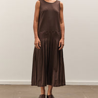 Woman wearing a brown sleeveless top and pleated skirt against a plain background