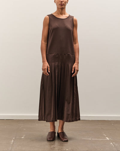 Woman wearing a brown sleeveless top and pleated skirt against a plain background