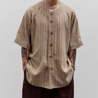 Man wearing a beige button-up shirt and dark pants against a plain background