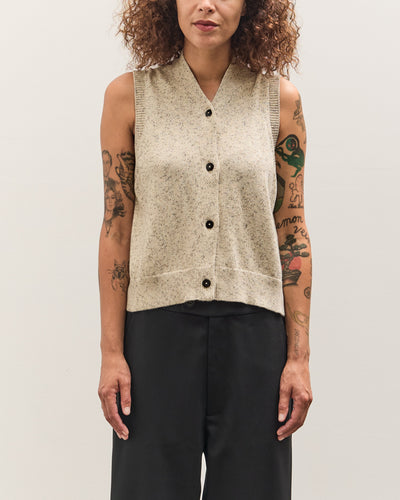 Person wearing a beige knitted vest with black buttons on a plain background