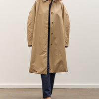 Person wearing a beige trench coat against a white background