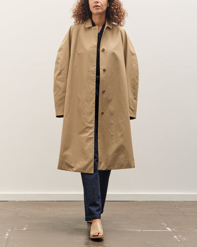 Person wearing a beige trench coat against a white background
