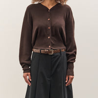Woman wearing a brown cardigan and dark pants against a plain background