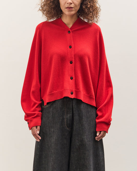Person wearing a red cardigan over a black top on a plain background