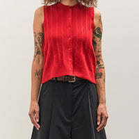 Person wearing a red sleeveless shirt and black pants on a plain background