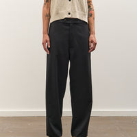 Person wearing black pants and a beige top against a white wall.