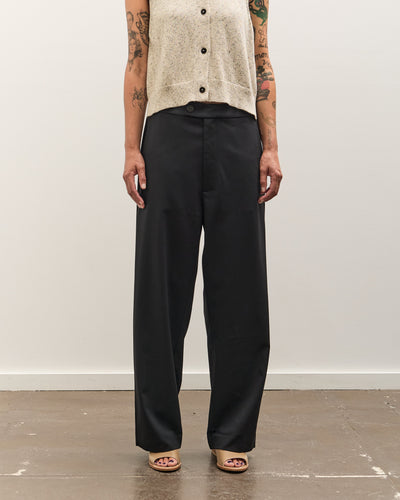 Person wearing black pants and a beige top against a white wall.