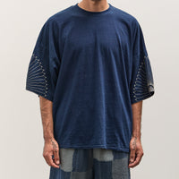 Man wearing a blue t-shirt with unique sleeve designs on a plain background