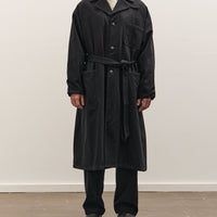 Man wearing a black coat standing against a white wall