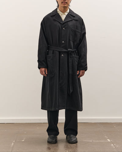 Man wearing a black coat standing against a white wall