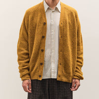 Man wearing a mustard yellow cardigan over a white shirt on a plain background