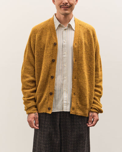 Man wearing a mustard yellow cardigan over a white shirt on a plain background