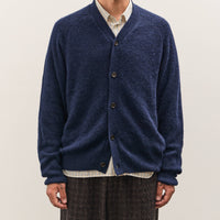 Man wearing a blue cardigan over a white shirt on a plain background