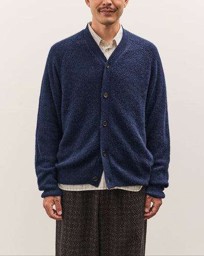 Man wearing a blue cardigan over a white shirt on a plain background