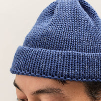 Man wearing a blue knitted beanie against a plain background
