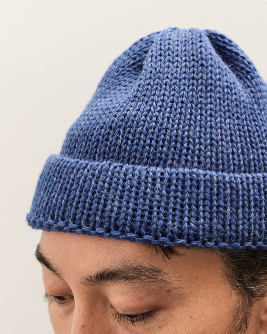 Man wearing a blue knitted beanie against a plain background