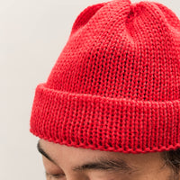 Person wearing a red knit beanie against a plain background