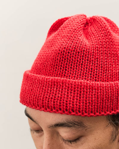 Person wearing a red knit beanie against a plain background